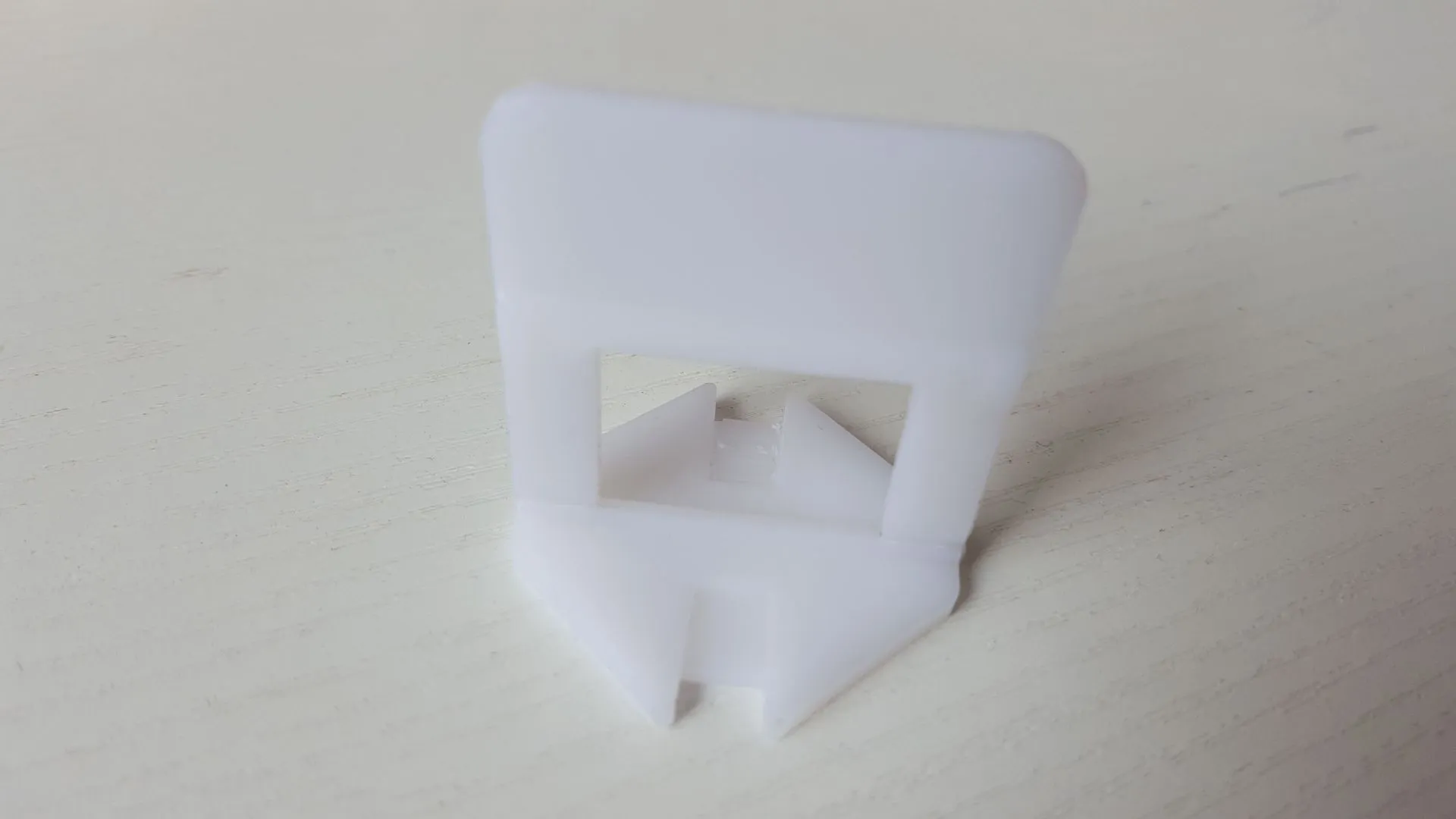 Orange plastic tile leveling wedges and white base clips on a tiled floor, with a rubber hammer nearby