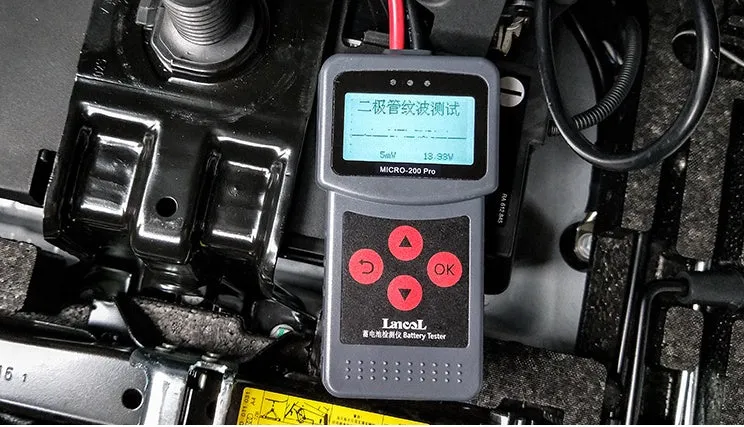 Black car battery tester with digital display measuring internal resistance on a workbench