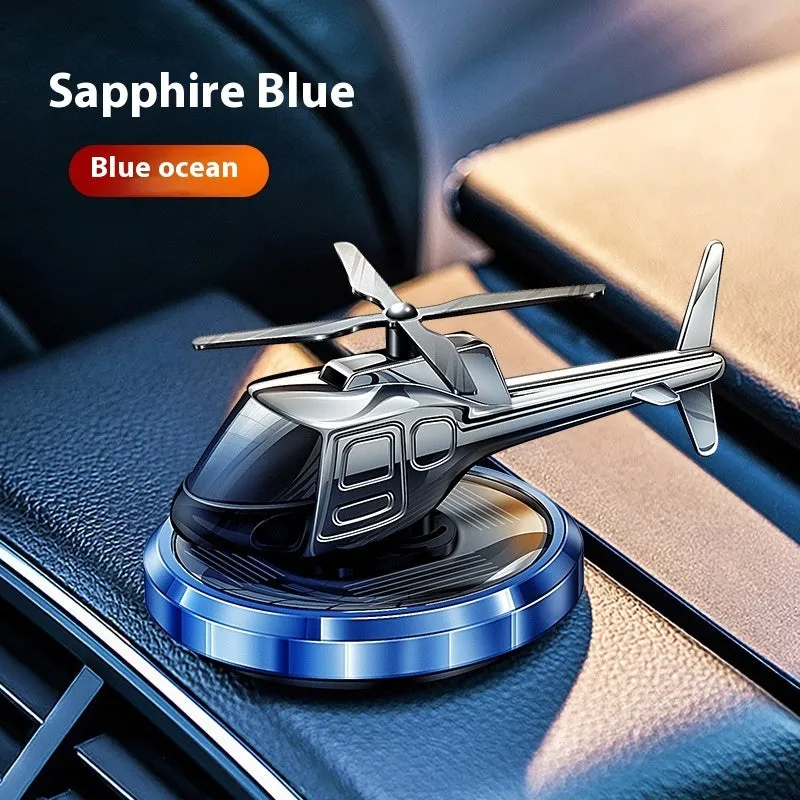 Silver solar-powered metal helicopter car air freshener ornament with spinning blades on a dashboard.
