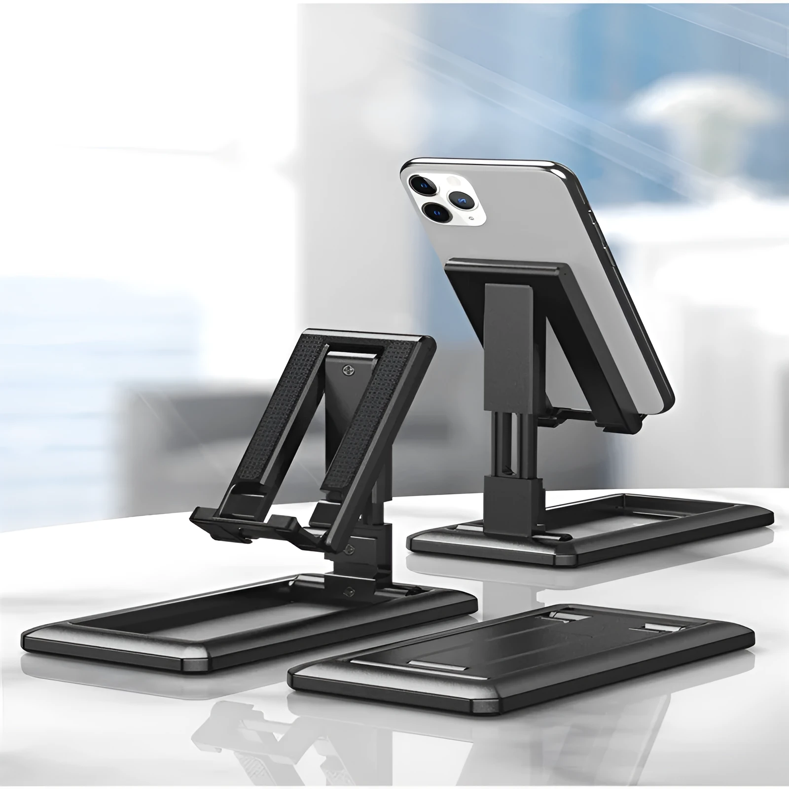 A folded and unfolded view of a black retractable mobile phone desktop stand on a wooden desk.