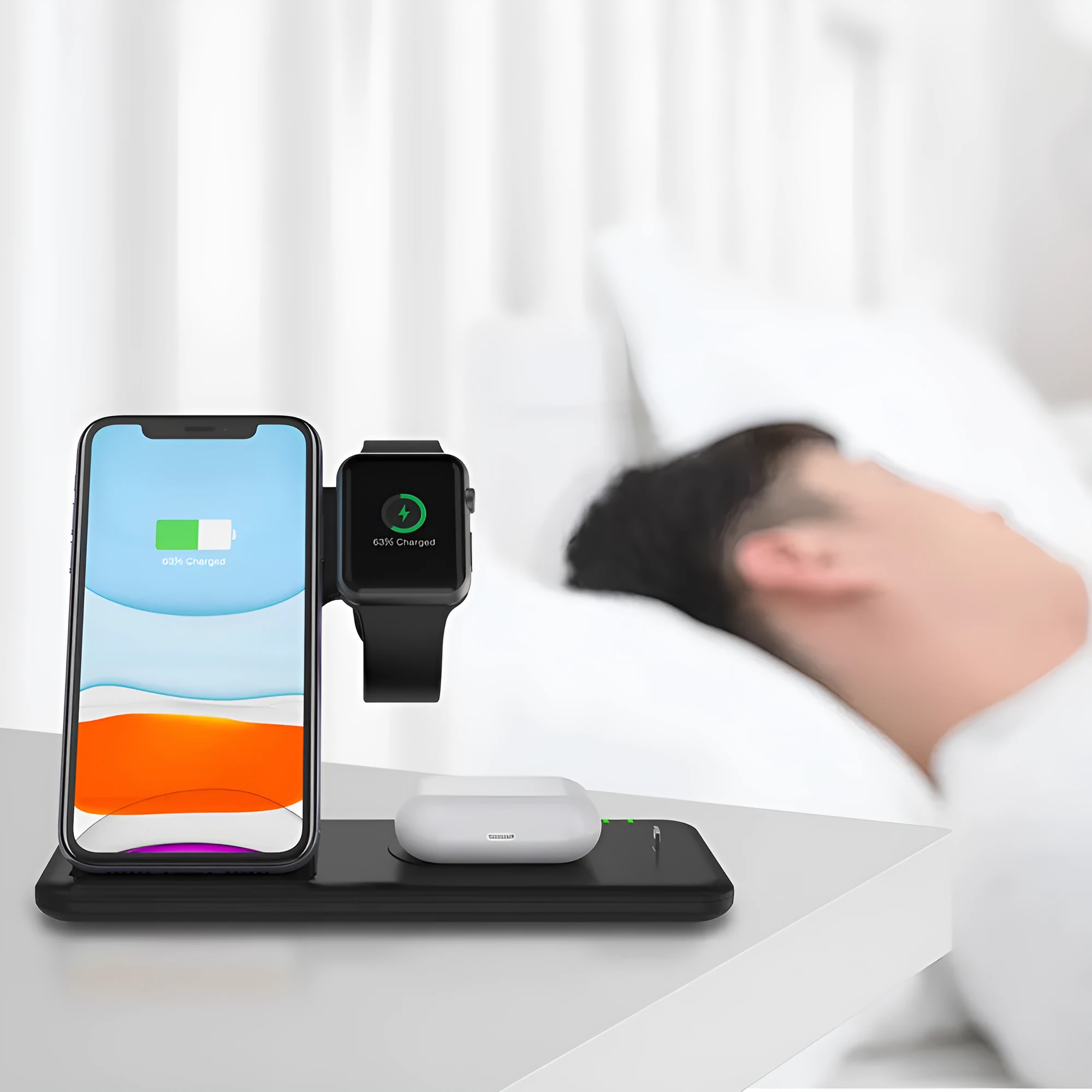 A white three-in-one wireless charging stand on a desk, charging a mobile phone, a smartwatch, and a pair of wireless headphones.