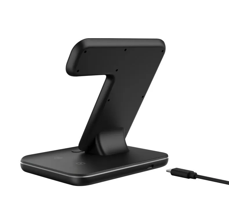 A white three-in-one wireless charging stand on a desk, charging a mobile phone, a smartwatch, and a pair of wireless headphones.