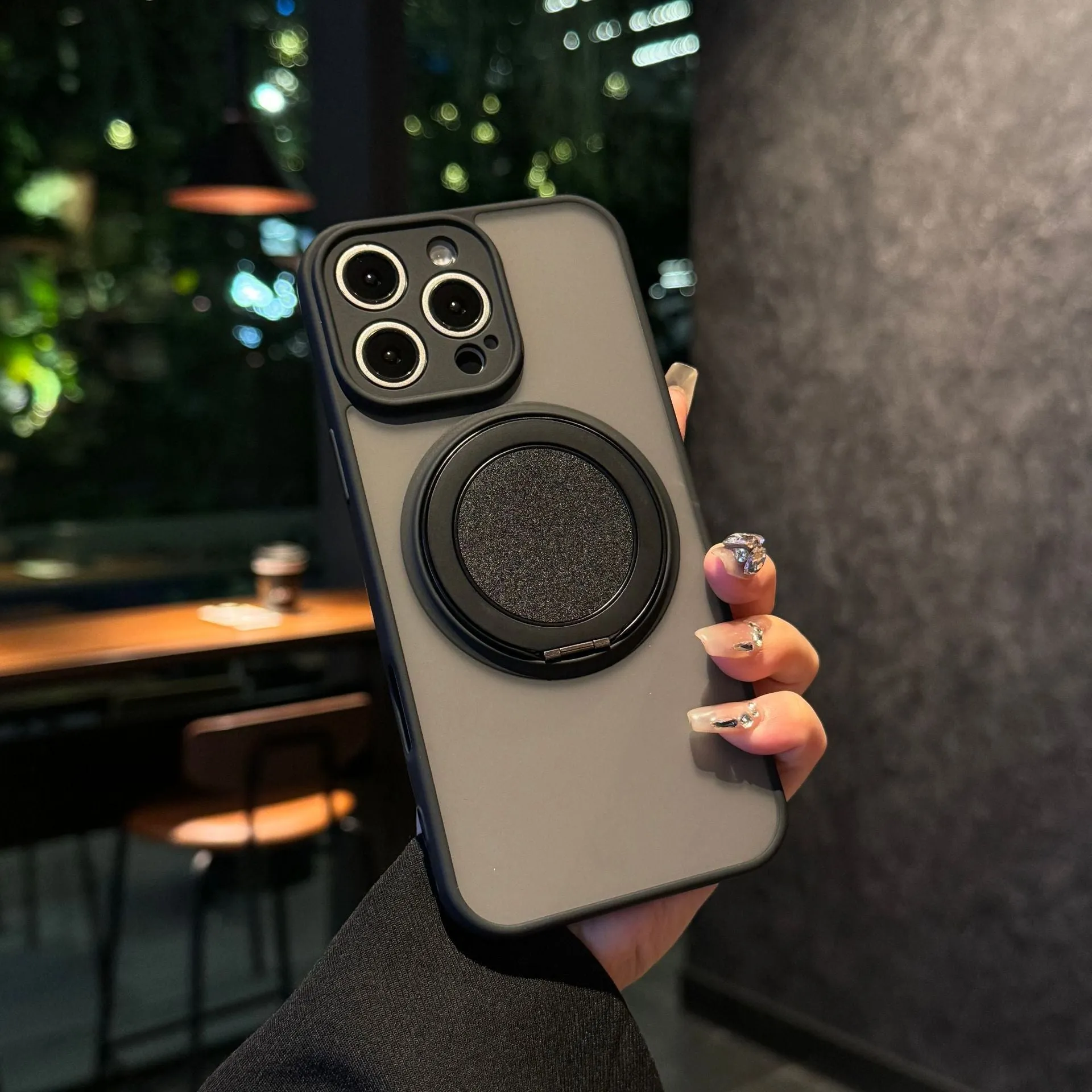Black frosted phone case for iPhone 17 with a rotating kickstand extended and visible magnetic ring on the back.