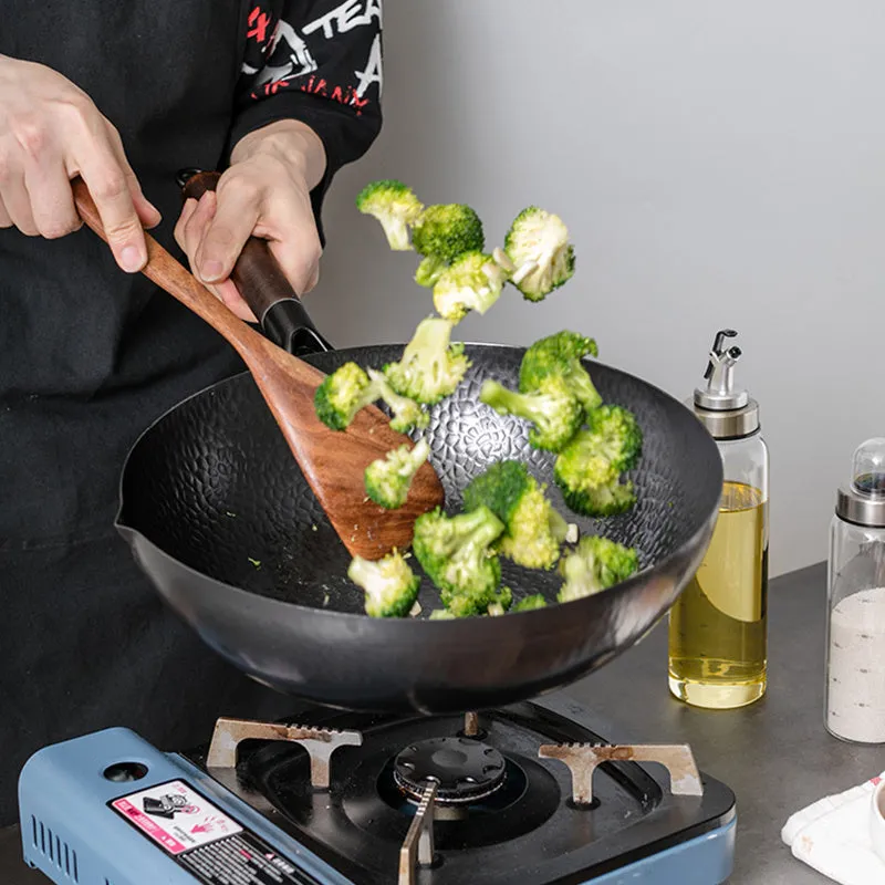 Handmade traditional black iron wok with a wooden handle, shown with a glass lid.