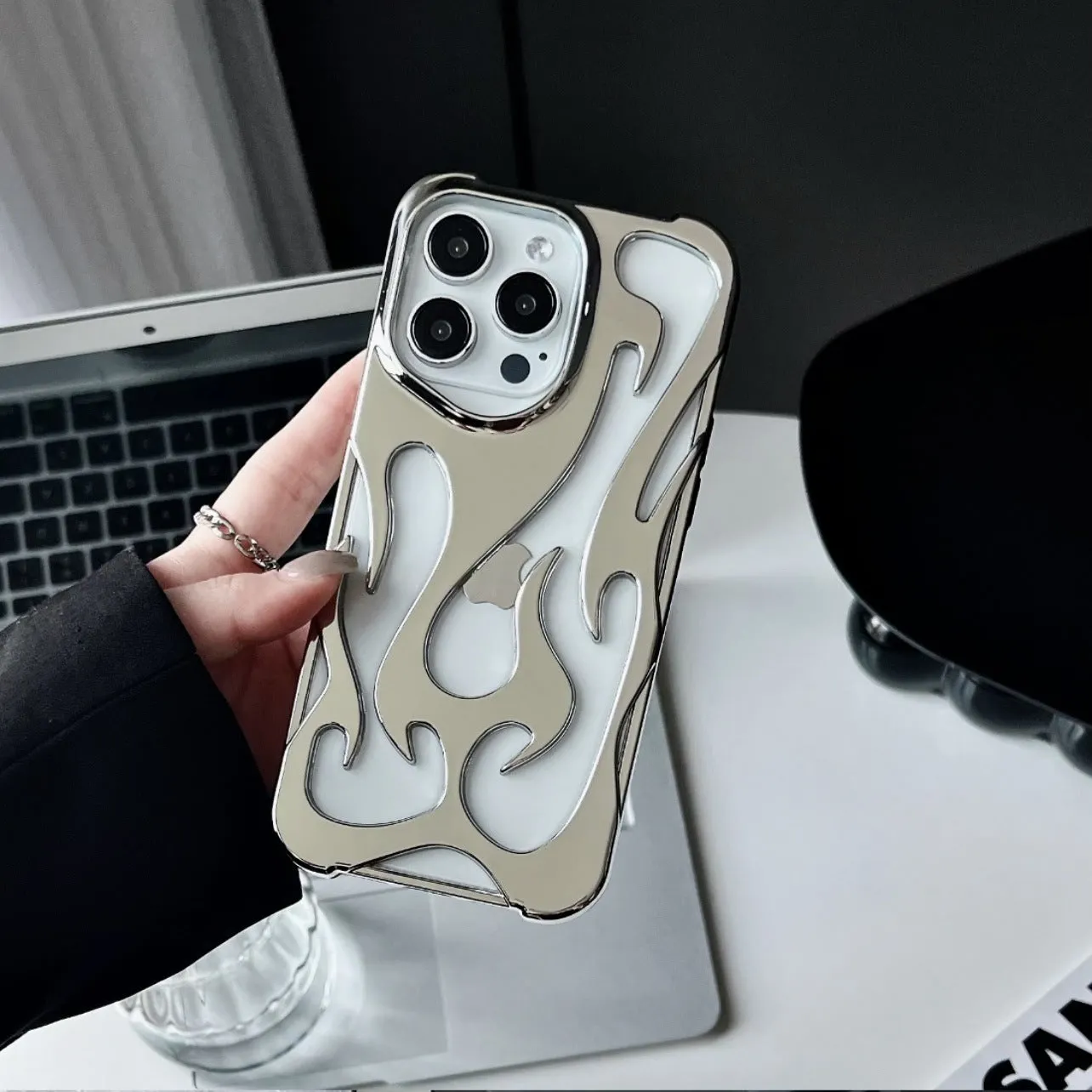 Electroplated hollow flame pattern TPU phone case for iPhone on a table, showing silver metallic finish and ventilation design.