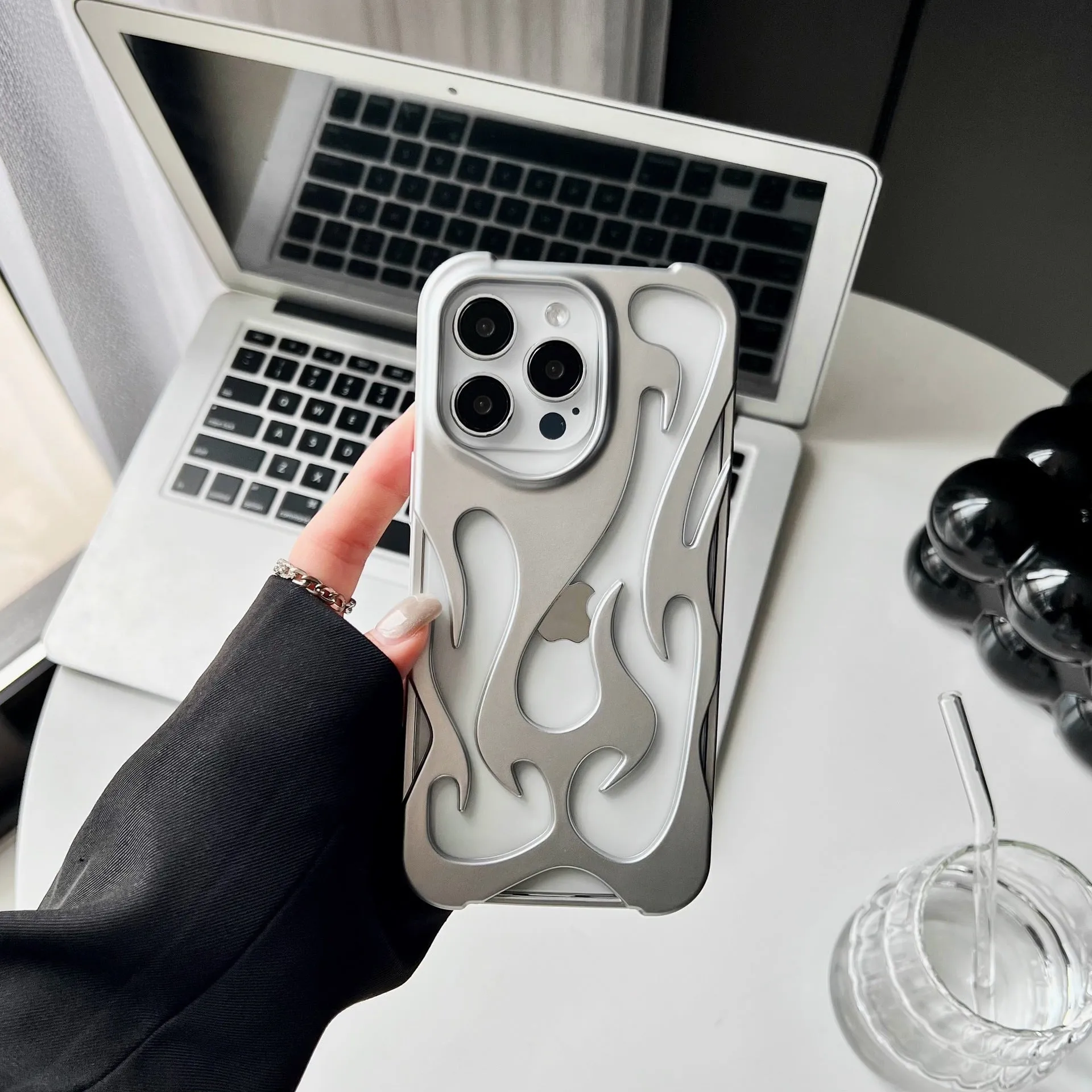 Electroplated hollow flame pattern TPU phone case for iPhone on a table, showing silver metallic finish and ventilation design.