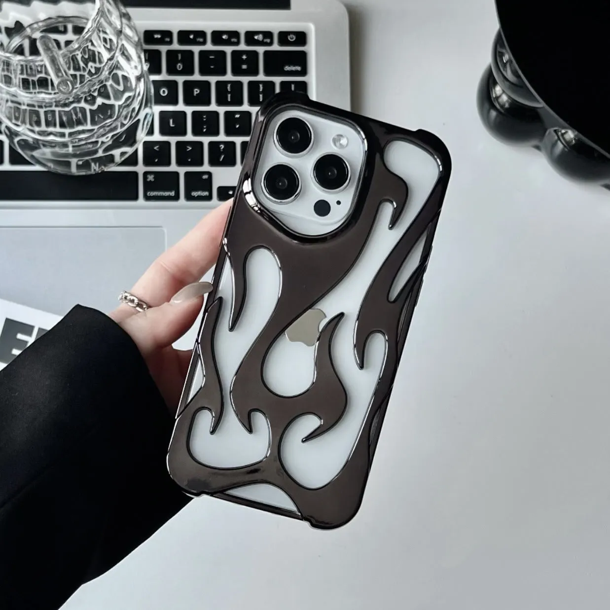 Electroplated hollow flame pattern TPU phone case for iPhone on a table, showing silver metallic finish and ventilation design.