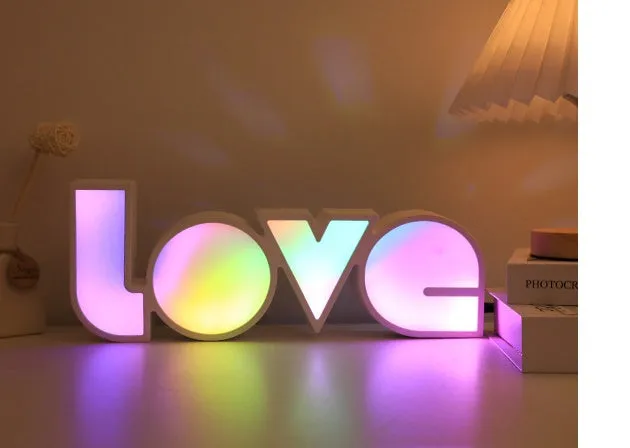 Rainbow style plastic LED decorative light spelling LOVE, shown on a table.