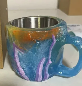 A purple resin coffee mug with a handle, showing a crystal-like structure, on a table.
