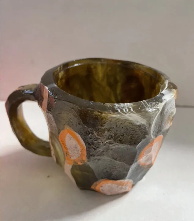 A purple resin coffee mug with a handle, showing a crystal-like structure, on a table.