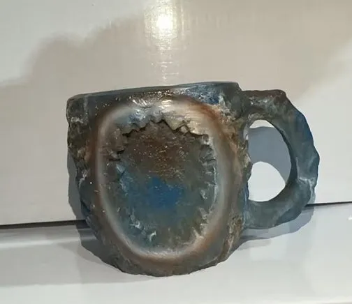 A purple resin coffee mug with a handle, showing a crystal-like structure, on a table.