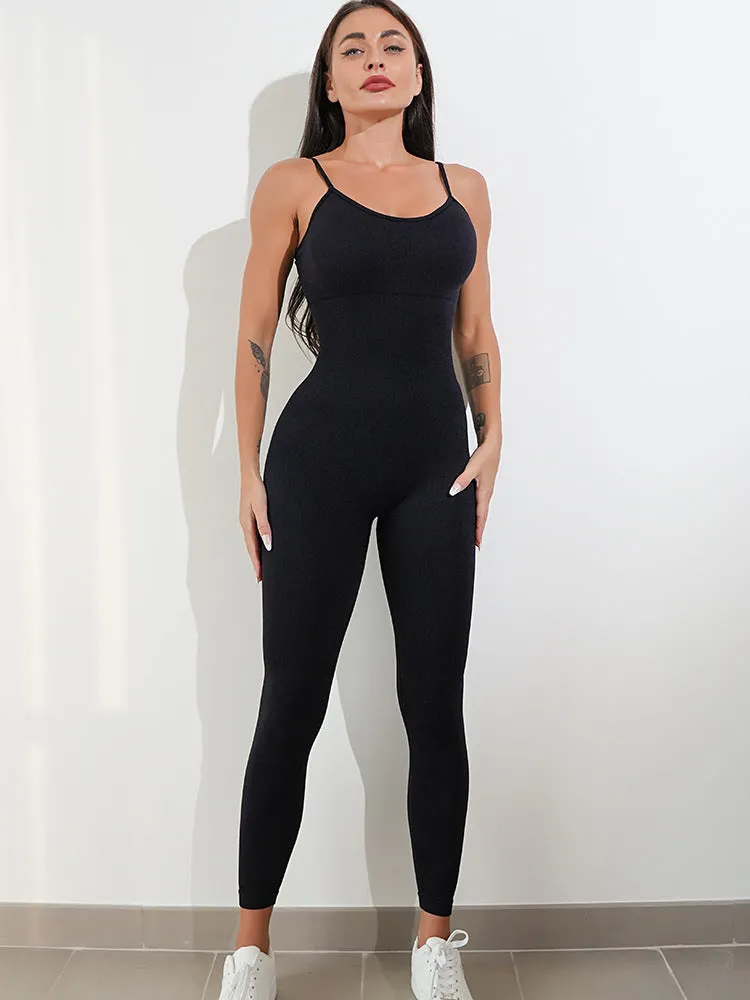 A woman wearing a black sleeveless unitard jumpsuit with spaghetti straps, showing the one-piece design and tummy control panel.