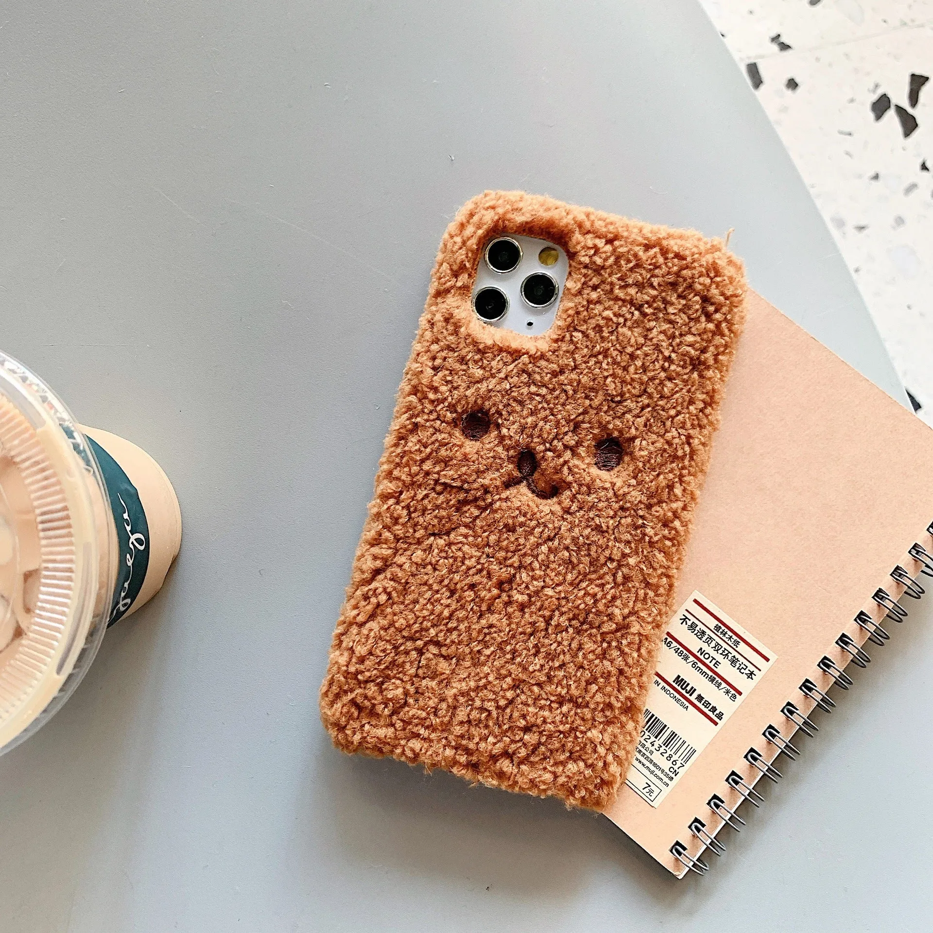 Brown embroidered plush cartoon bear face on a flexible TPU iPhone case.
