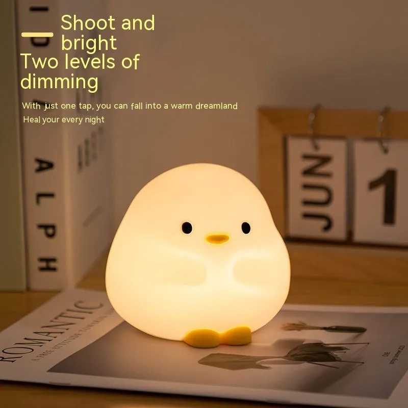 Cute duck shaped LED night lamp with silicone casing and warm light on a bedside table