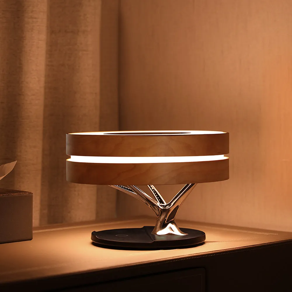 Round maple-coloured ABS PC Bluetooth speaker lamp with LED tree ring and wireless charging pad on a bedside table