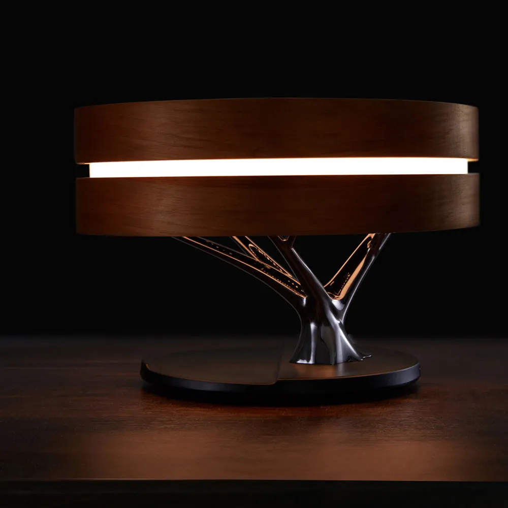 Round maple-coloured ABS PC Bluetooth speaker lamp with LED tree ring and wireless charging pad on a bedside table