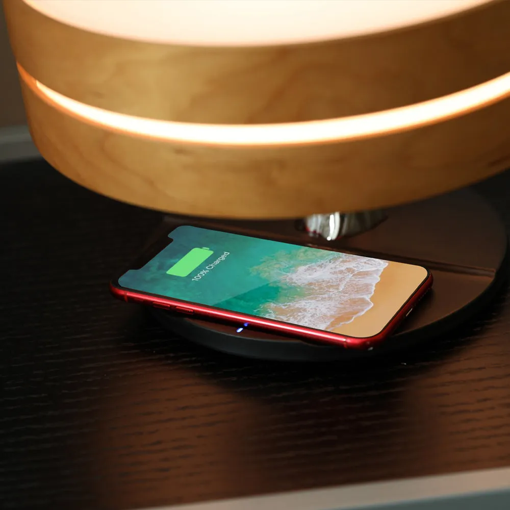 Round maple-coloured ABS PC Bluetooth speaker lamp with LED tree ring and wireless charging pad on a bedside table