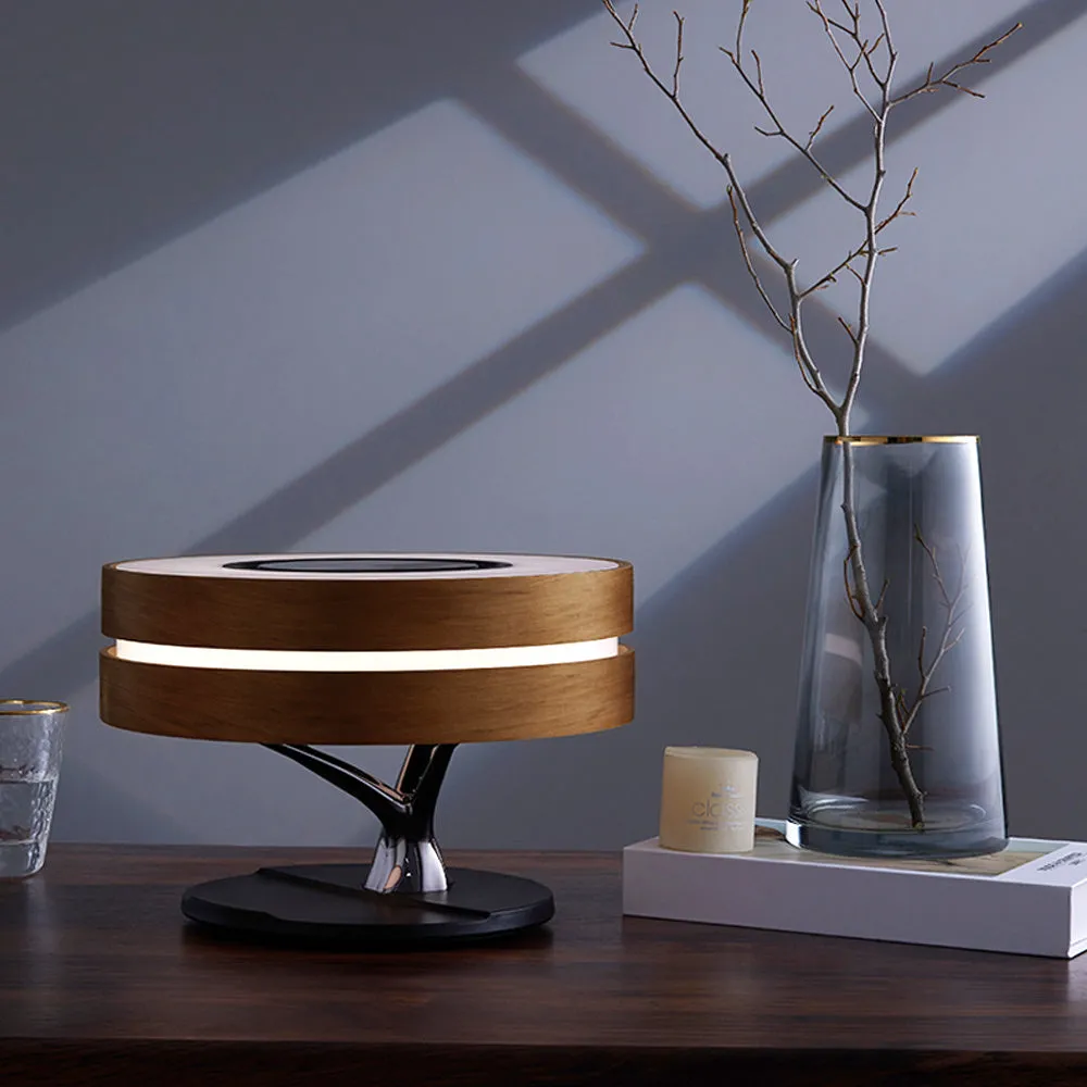 Round maple-coloured ABS PC Bluetooth speaker lamp with LED tree ring and wireless charging pad on a bedside table