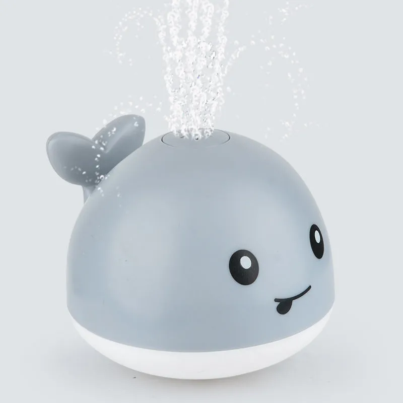 White and blue whale bath toy spraying water with LED lights on, floating in a bathtub
