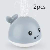 White and blue whale bath toy spraying water with LED lights on, floating in a bathtub