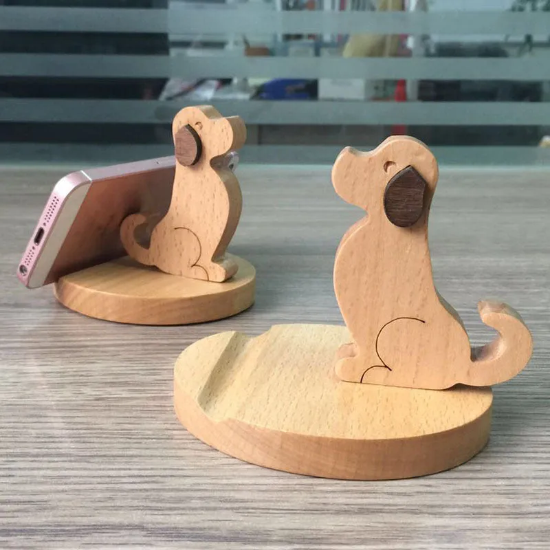 Solid wood cartoon puppy phone bracket with brown spray paint on a desk holding a smartphone upright.