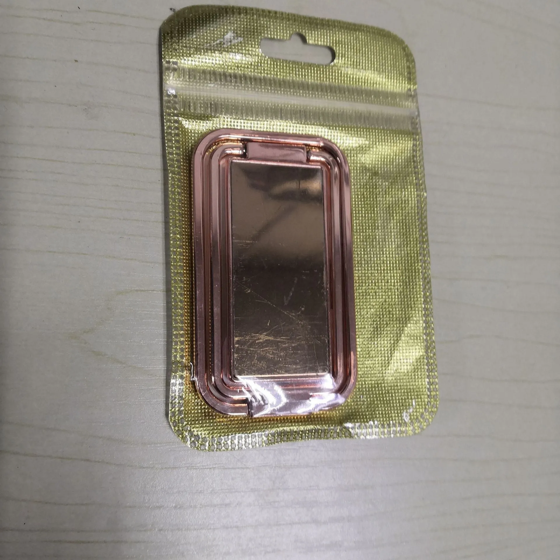 Folding double ring metal phone holder in silver with square buckle, open on a desk holding a smartphone