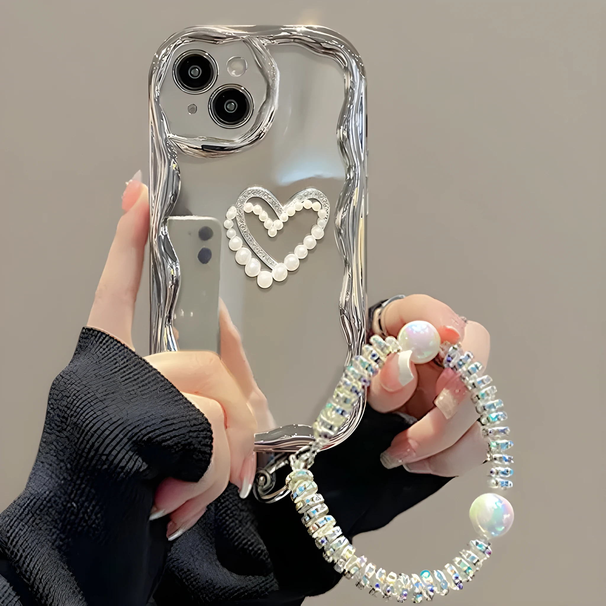 Silver grey silicone phone case for iPhone 15 Pro Max with three-dimensional pearls and chain, electroplated finish, and matching bracelet on a table