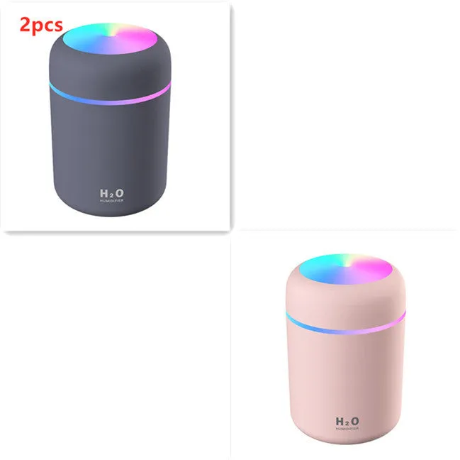 Pink USB desktop humidifier with coloured LED lights and water tank on a wooden desk.