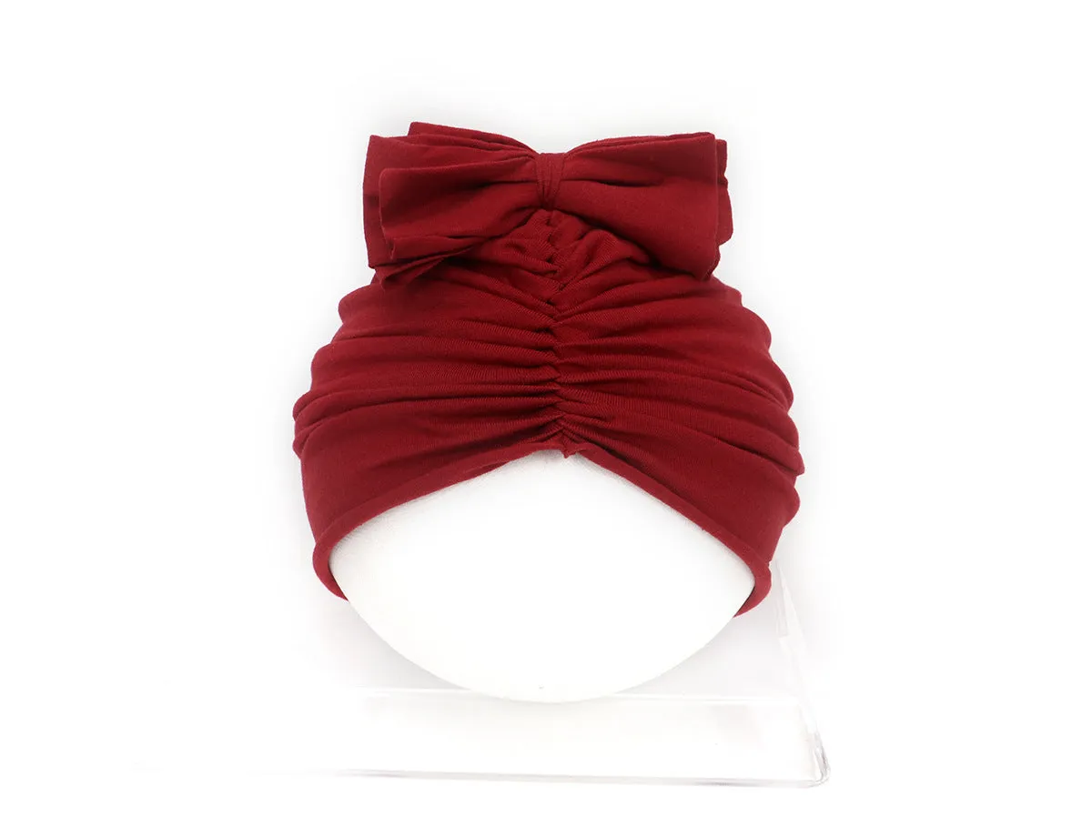 Baby girl wearing a soft, knitted purple turban-style hat on a white background.