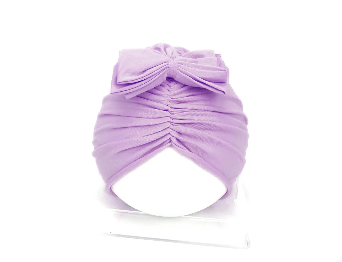 Baby girl wearing a soft, knitted purple turban-style hat on a white background.