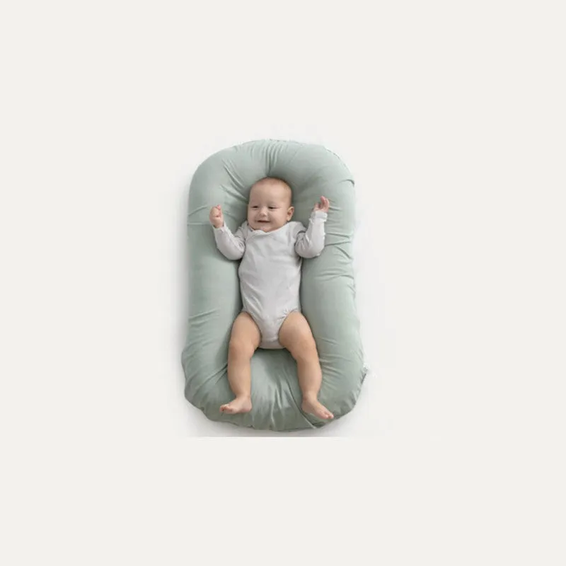 Cotton portable baby nest crib for newborns, beige colour, shown on a bed.