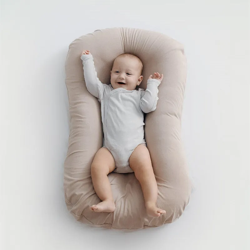 Cotton portable baby nest crib for newborns, beige colour, shown on a bed.