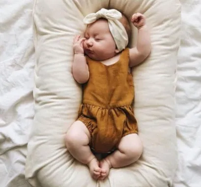 Cotton portable baby nest crib for newborns, beige colour, shown on a bed.