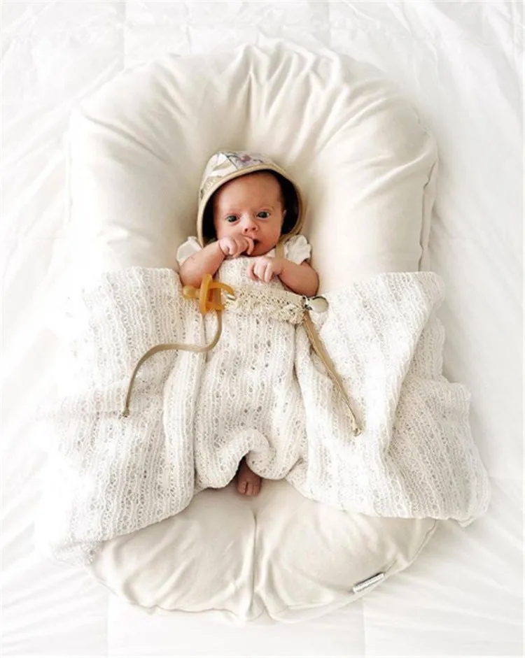 Cotton portable baby nest crib for newborns, beige colour, shown on a bed.