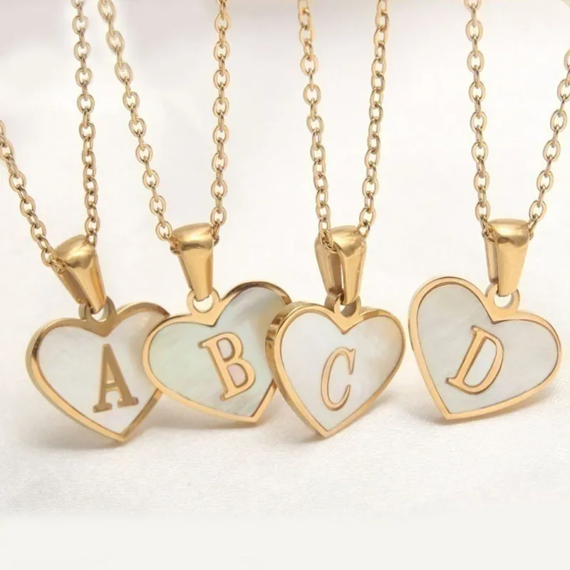 Gold-plated heart-shaped white shell initial necklace on a model, showing the adjustable clavicle chain.