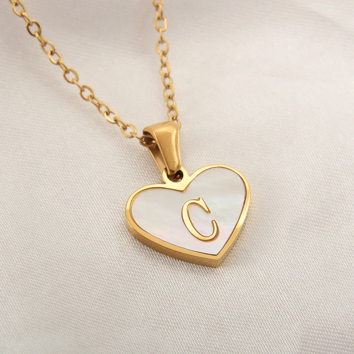Gold-plated heart-shaped white shell initial necklace on a model, showing the adjustable clavicle chain.