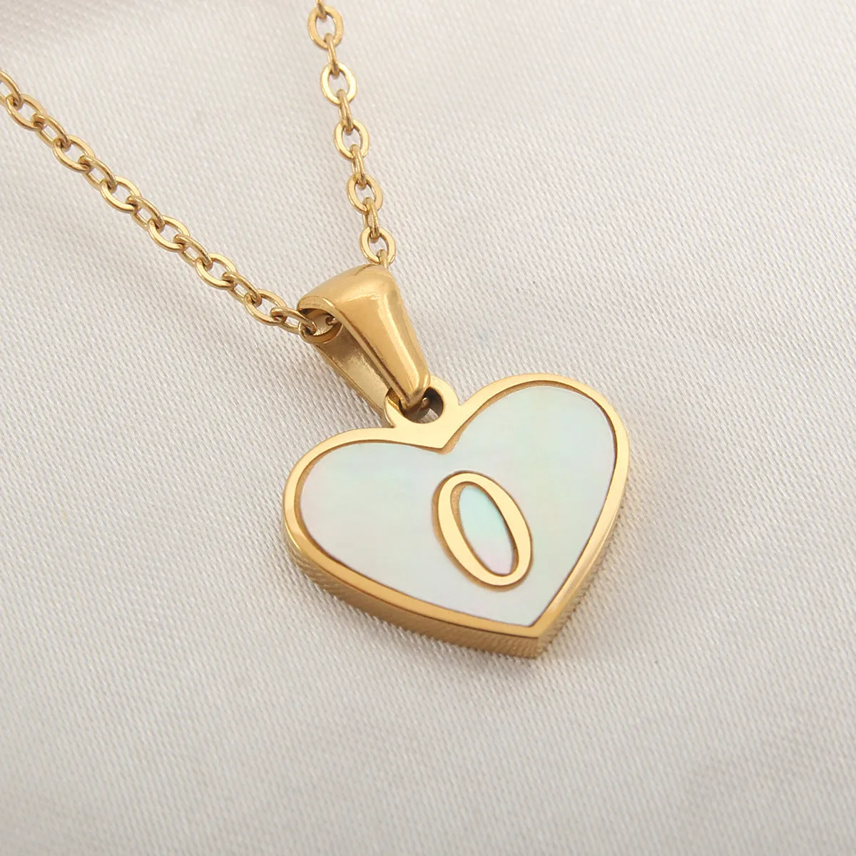 Gold-plated heart-shaped white shell initial necklace on a model, showing the adjustable clavicle chain.