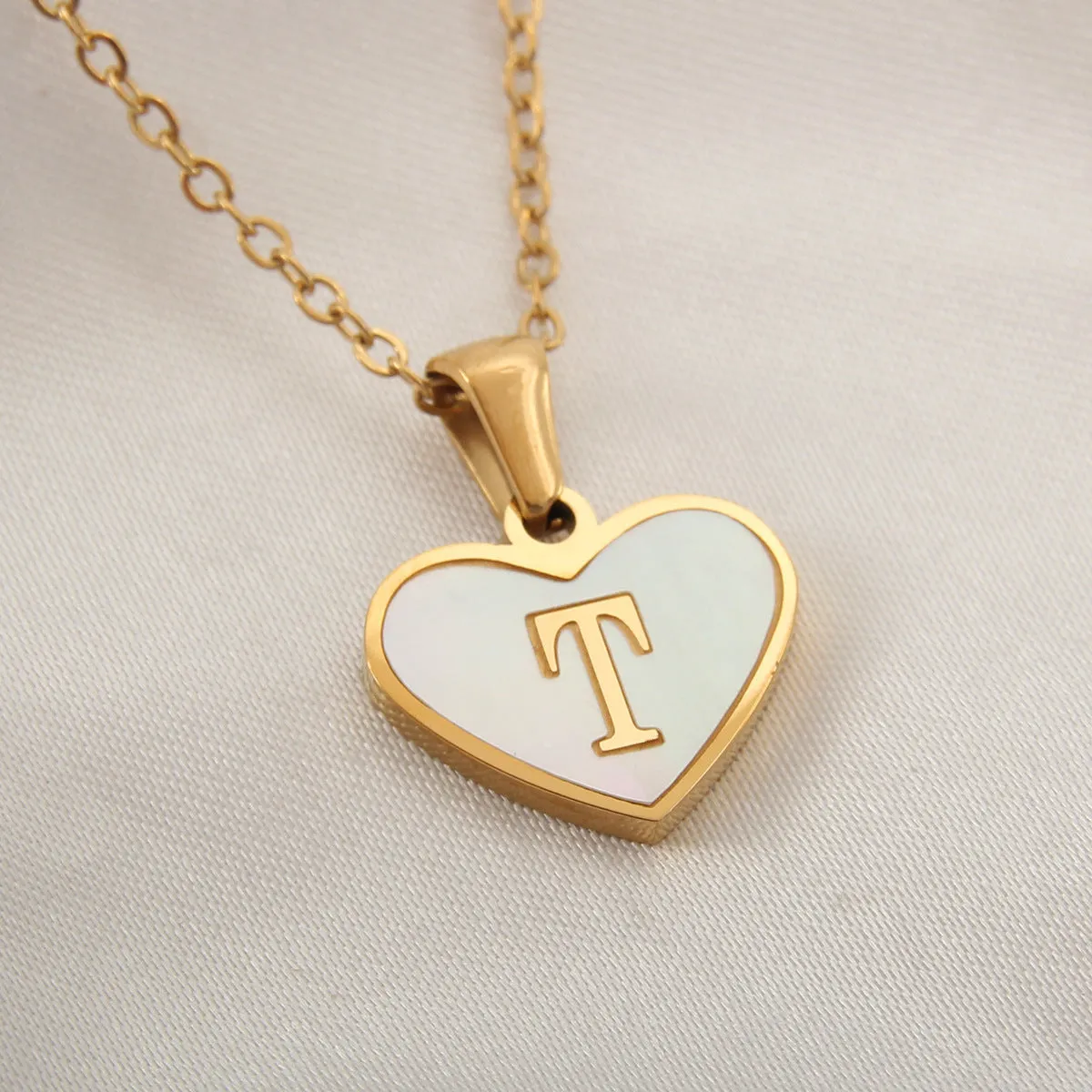 Gold-plated heart-shaped white shell initial necklace on a model, showing the adjustable clavicle chain.