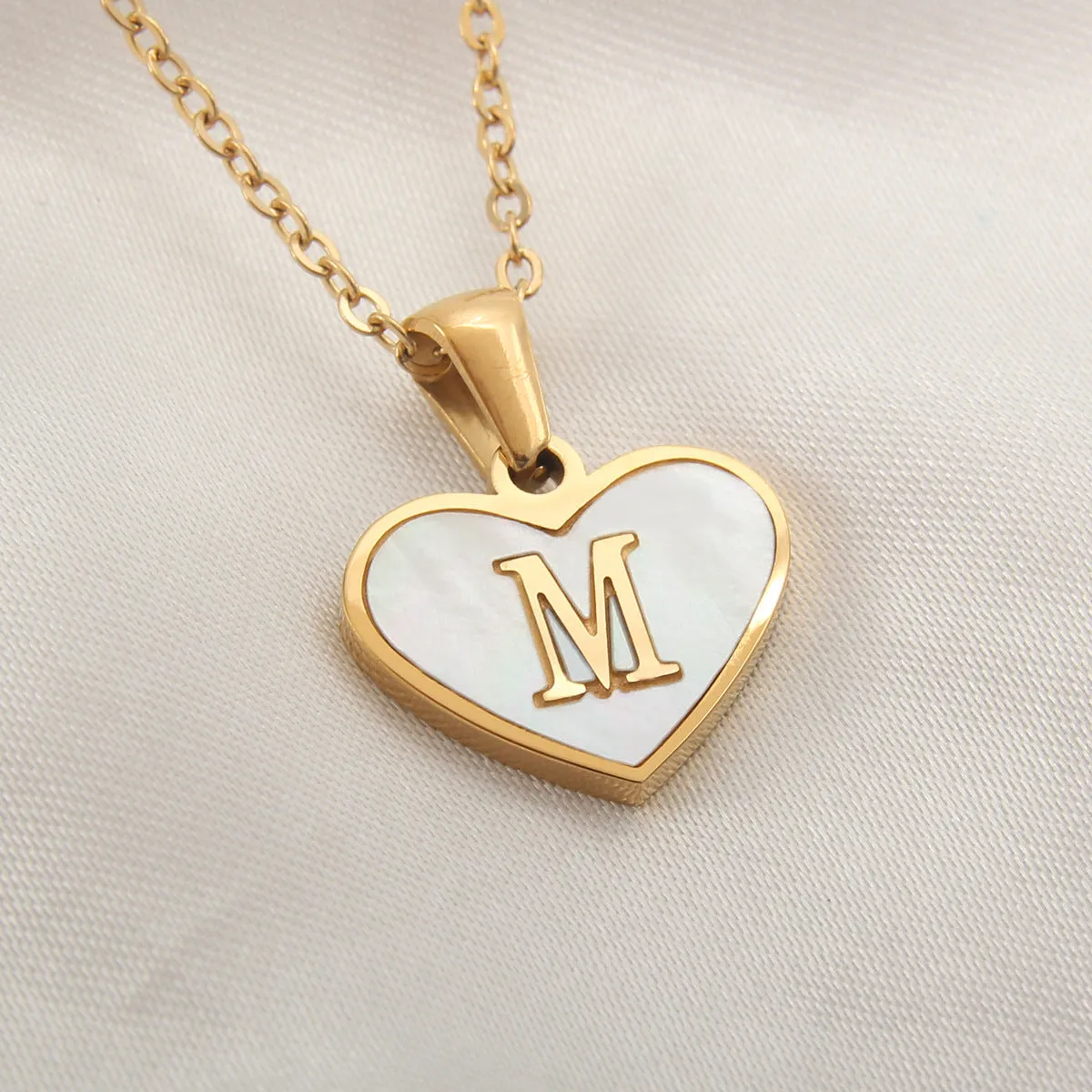 Gold-plated heart-shaped white shell initial necklace on a model, showing the adjustable clavicle chain.