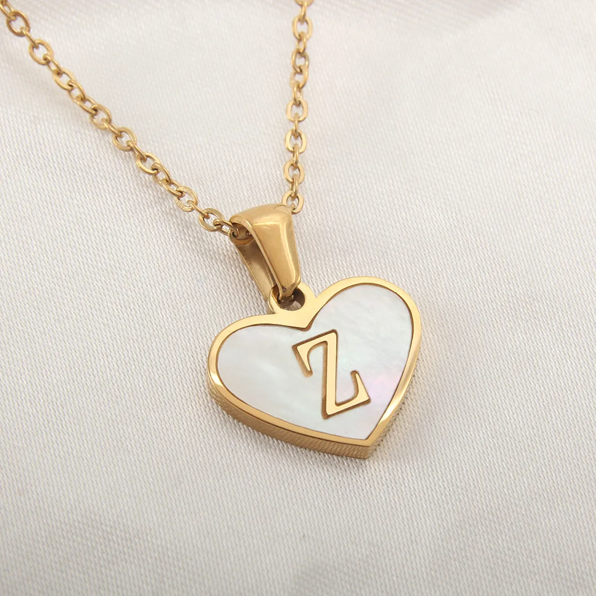 Gold-plated heart-shaped white shell initial necklace on a model, showing the adjustable clavicle chain.