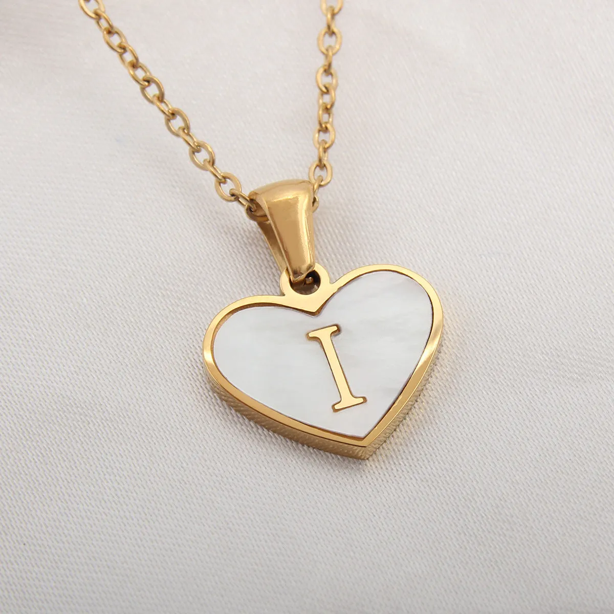 Gold-plated heart-shaped white shell initial necklace on a model, showing the adjustable clavicle chain.