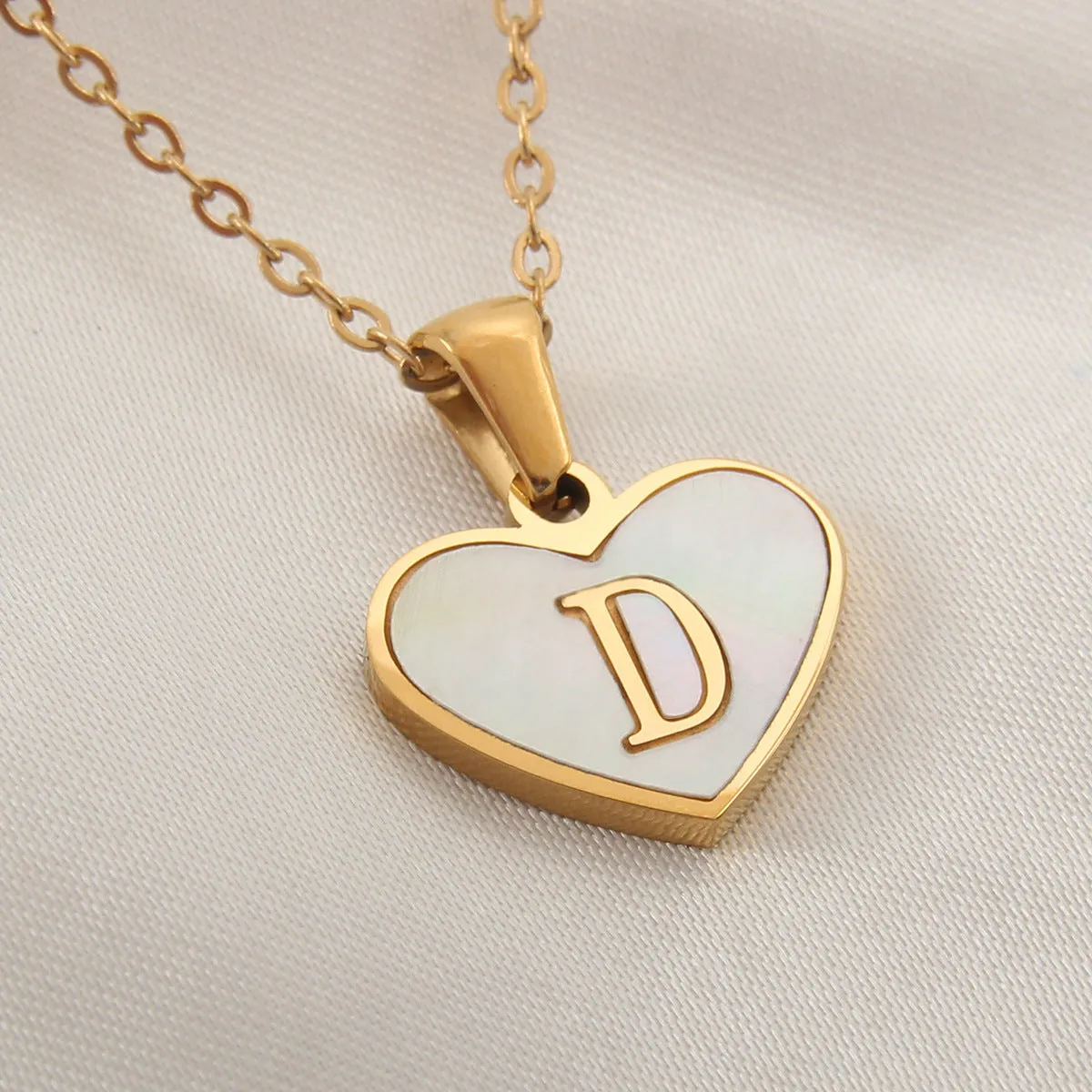 Gold-plated heart-shaped white shell initial necklace on a model, showing the adjustable clavicle chain.