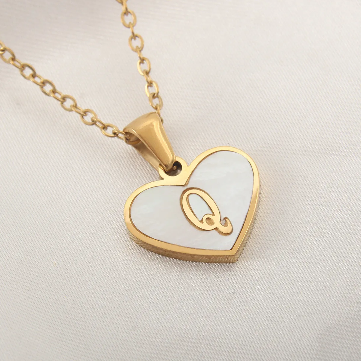 Gold-plated heart-shaped white shell initial necklace on a model, showing the adjustable clavicle chain.