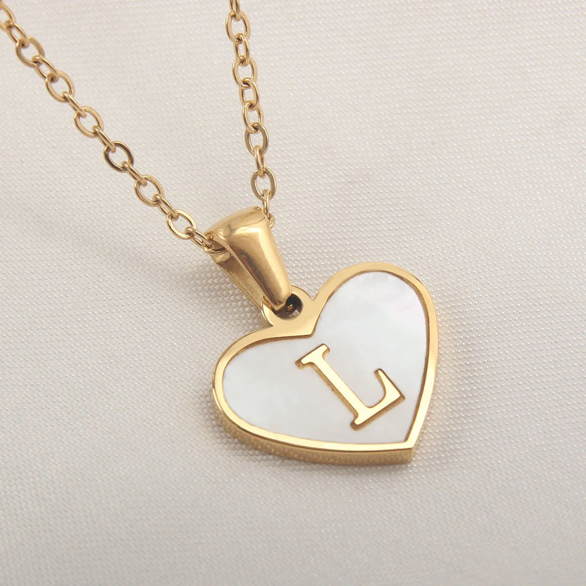 Gold-plated heart-shaped white shell initial necklace on a model, showing the adjustable clavicle chain.