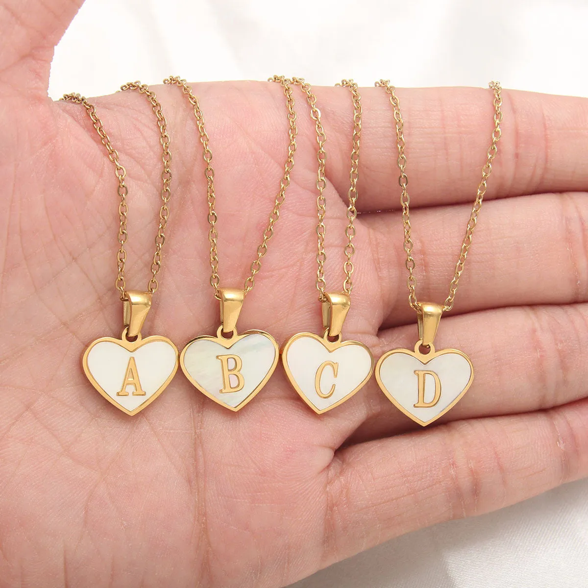 Gold-plated heart-shaped white shell initial necklace on a model, showing the adjustable clavicle chain.