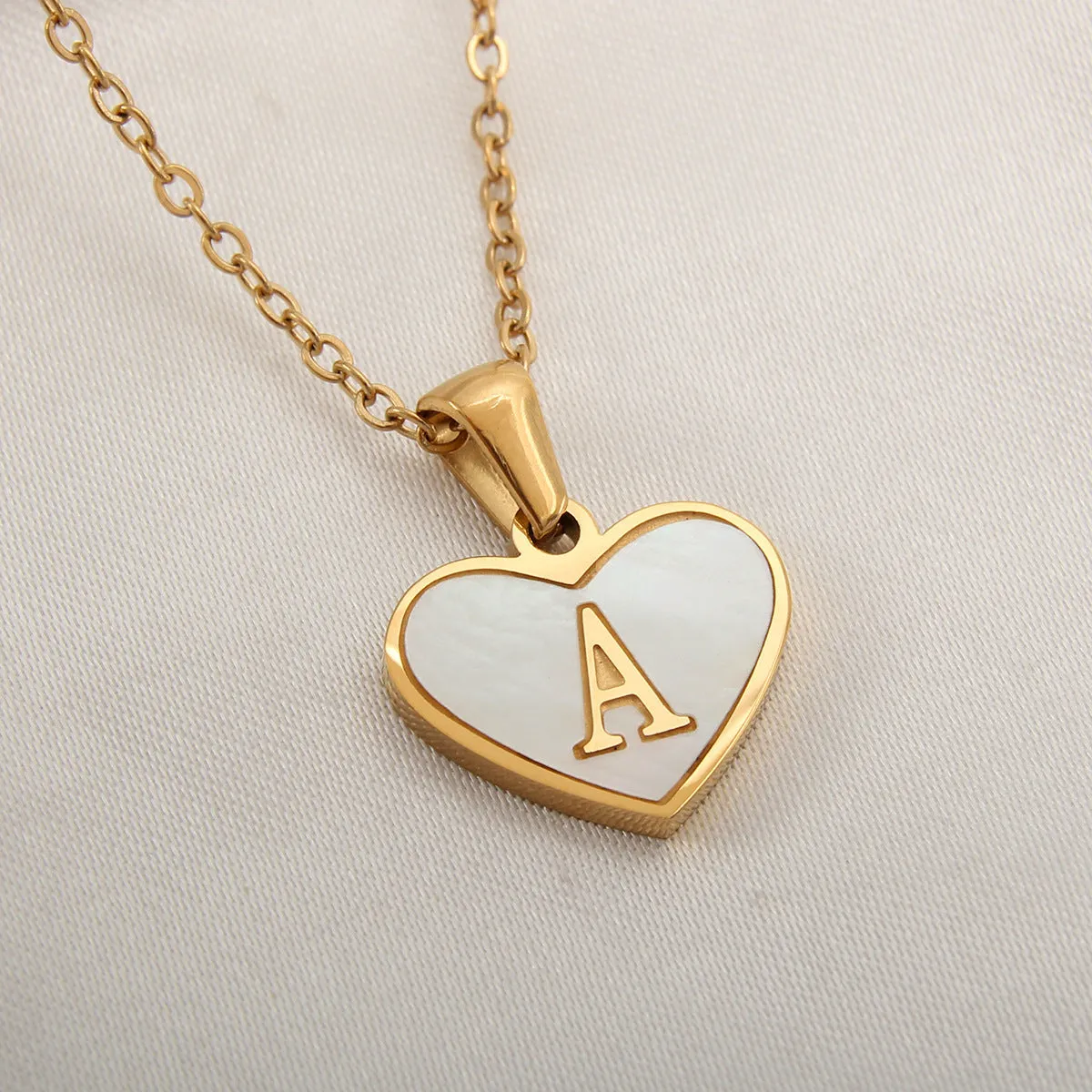 Gold-plated heart-shaped white shell initial necklace on a model, showing the adjustable clavicle chain.
