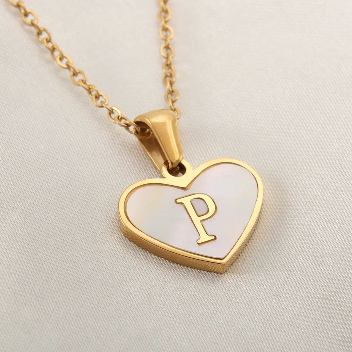 Gold-plated heart-shaped white shell initial necklace on a model, showing the adjustable clavicle chain.