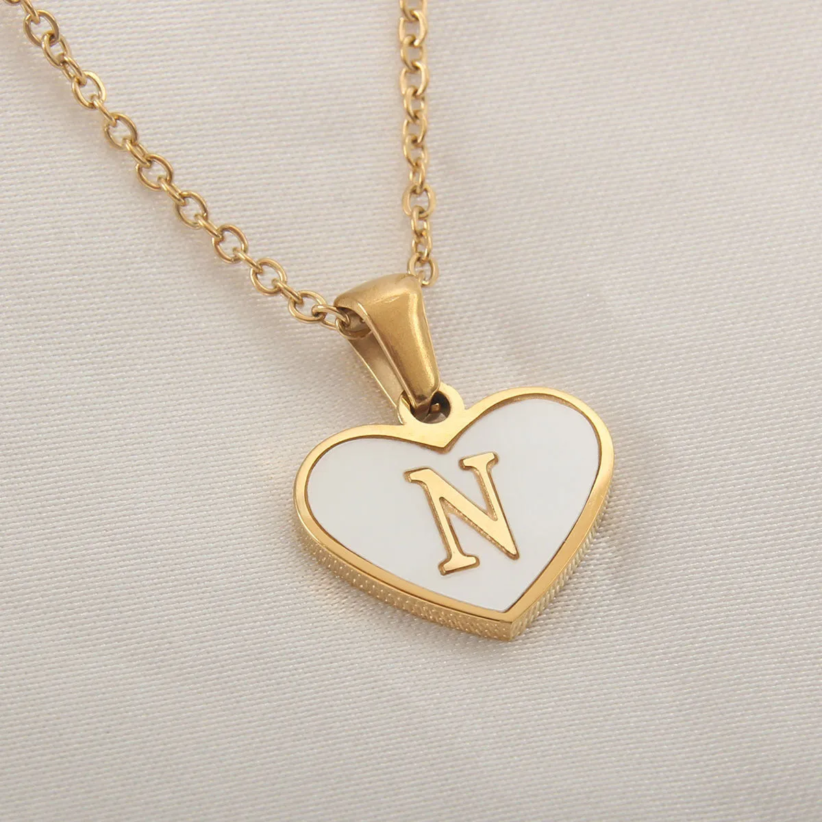 Gold-plated heart-shaped white shell initial necklace on a model, showing the adjustable clavicle chain.