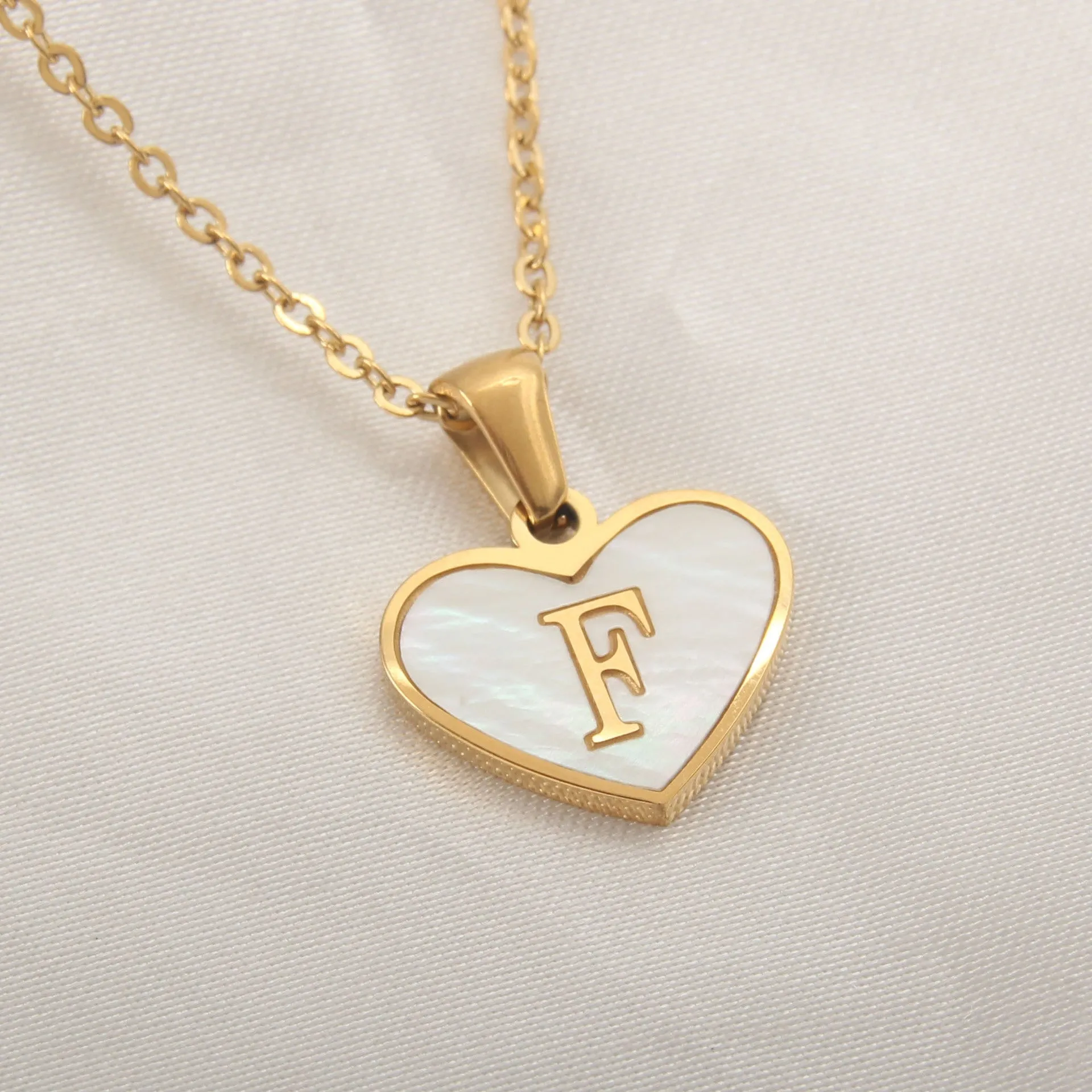 Gold-plated heart-shaped white shell initial necklace on a model, showing the adjustable clavicle chain.