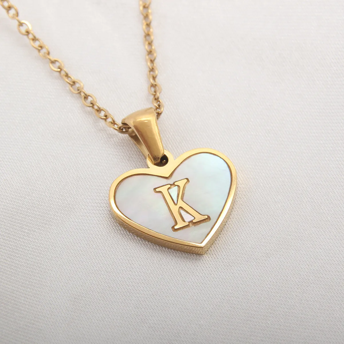Gold-plated heart-shaped white shell initial necklace on a model, showing the adjustable clavicle chain.